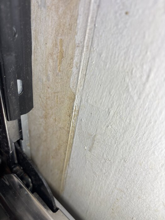 Närbild på en vitmålad yta med en täckskiva i hörnet, där färgen ser ojämn ut och potentiellt är dåligt målad.