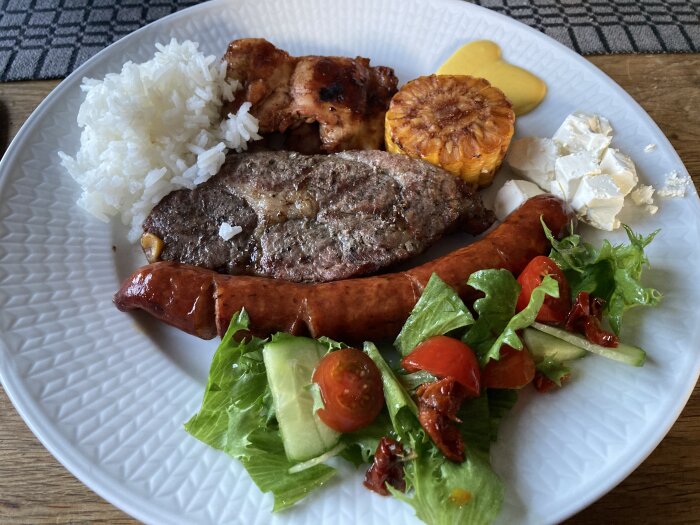 Tallrik med blandgrill: ris, grillad kyckling, majs, fetaost, korv, biff och sallad med tomat och gurka.