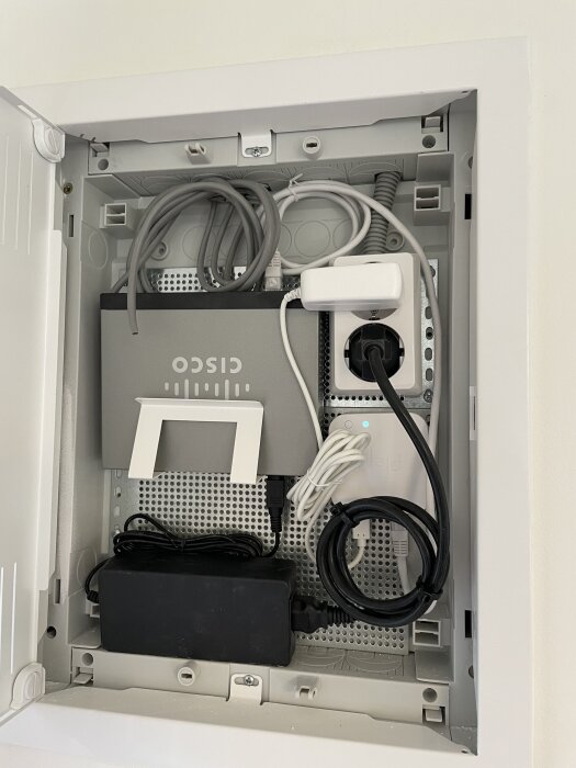 En nätverkscentral med en Cisco-enhet och flera kablar installerade på en vägg, en del av ett hemnätverksprojekt.