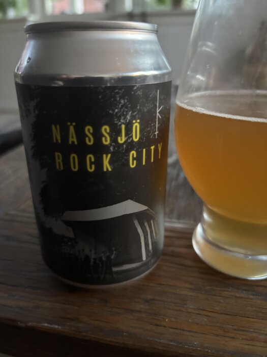 Burk med öl av märket Nässjö Rock City och ett glas med öl på ett träbord.