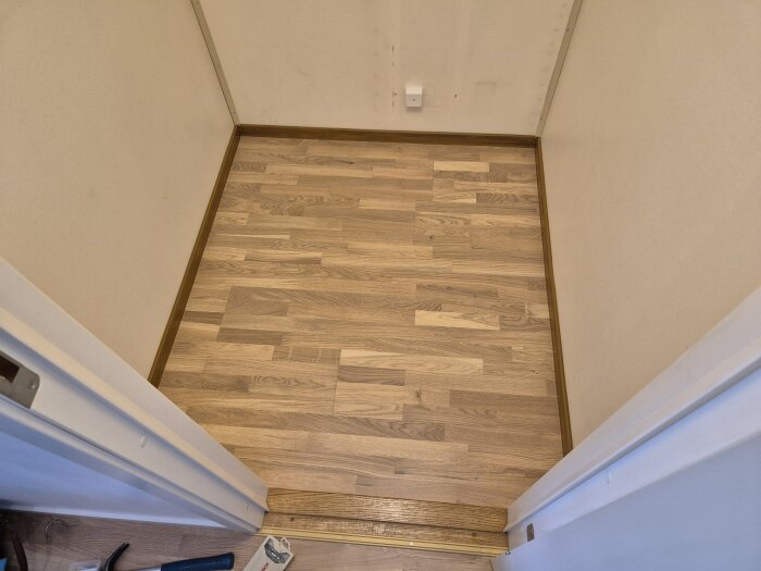 Klädkammare med nylagd parkettgolv, omgivna av vita väggar och återanvända bruna plastlister.