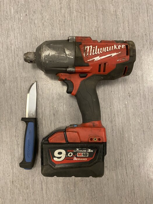 Bild av en röd Milwaukee batteridriven mutterdragare och en Mora-kniv på golvet.