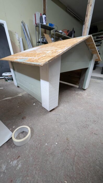 Miniatyrmodell av ett hus under konstruktion, med ett provisoriskt tak i trä; huset ska efterlikna ett bostadshus i miniatyr.