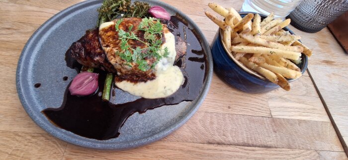 Grillad fläskkarréskiva med sparris, rödlök, sås och pommes kryddad med salt och persilja på en tallrik.