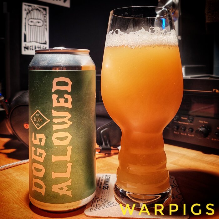 En burk med "Dogs Allowed" öl bredvid ett glas fyllt med skummande, gyllene öl, placerade på ett träbord.