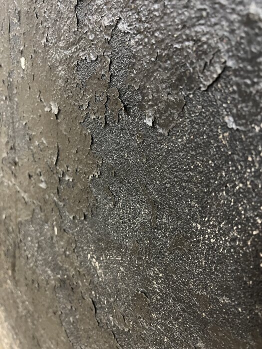 Flagnande svart färg på en putsad vägg, som visar underliggande lager där färg sitter fast i putsen, vilket skapar behov av renovering.