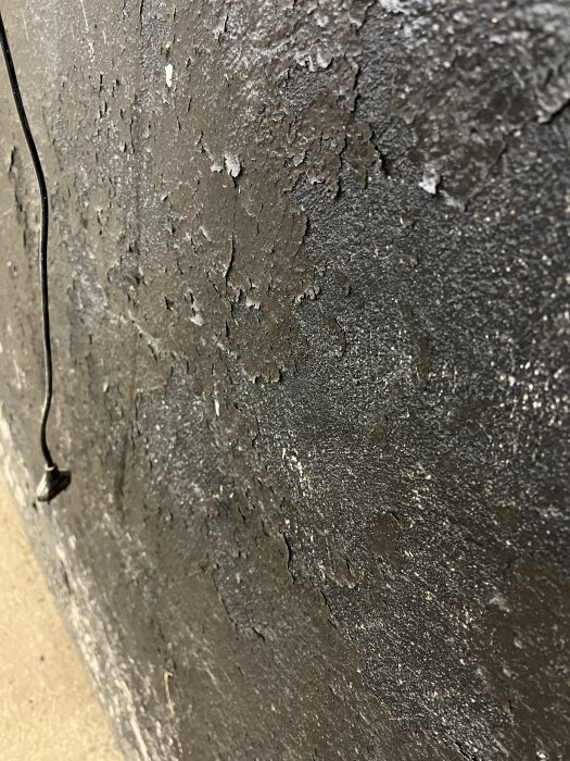 Flagad svart färg på vägg med underliggande murbruk synligt.