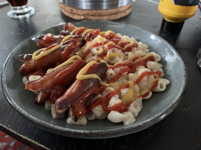 Tallrik med stuvade makaroner och prinskorv, toppad med ketchup och senap.