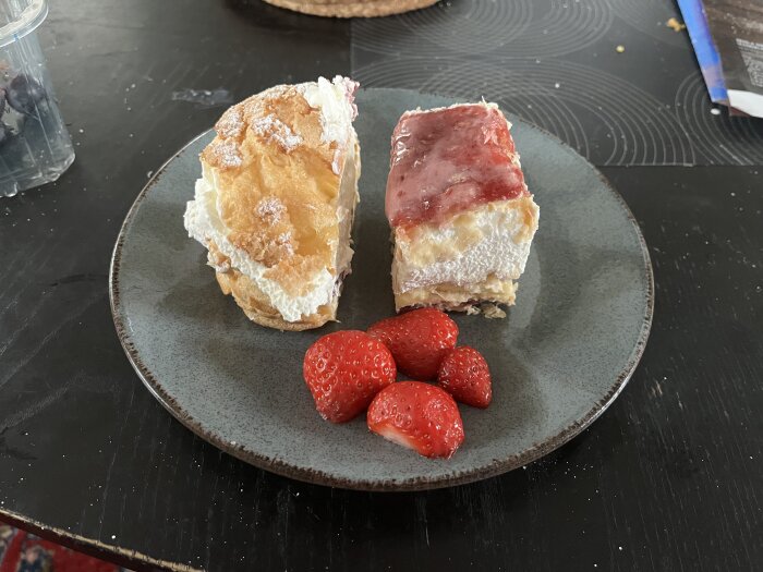 Två bakelser och några färska jordgubbar på ett grått fat, placerat på ett mörkt bord.