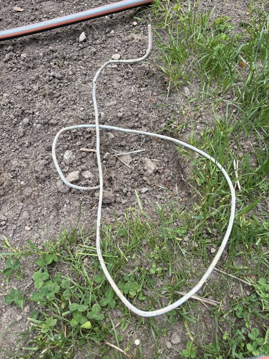 Gammal ljusblå kabel med två metalledare, grävd upp ur gräsmattan, ligger i jorden vid grönt gräs och jord.