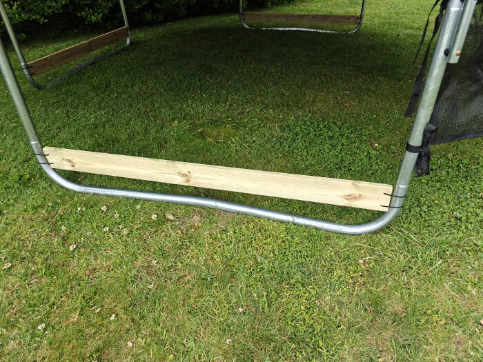 Träribba fäst vid metallram på grön gräsmatta; del av en överbyggnad eller konstruktion.