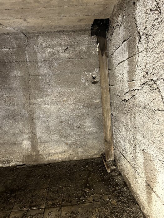 Fuktskadad vägg med sprickor, stöd av träregel och fuktigt golv i utrymme under balkong.