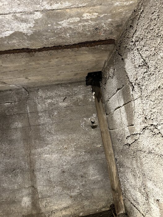 Rostigt armeringsjärn och fuktskadad regel under balkong, med fuktfläckar och sprickor i betongen.