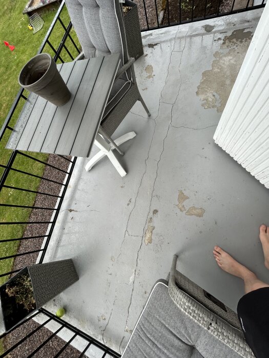 Betonggolv på balkong med sprickor och fuktskador; bord och stolar synliga; används för att belysa möjliga fuktkällor och behov av reparation.