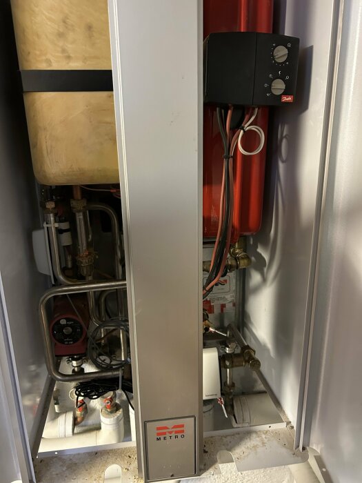 A district heating system unit with visible pipes, valves, and a control panel with dials.