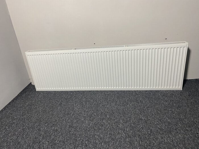 Radiator från Purmo, modell Thermopanel TP22, vit och i fint skick, cirka 200x60 cm, mot en vit vägg med grå matta.