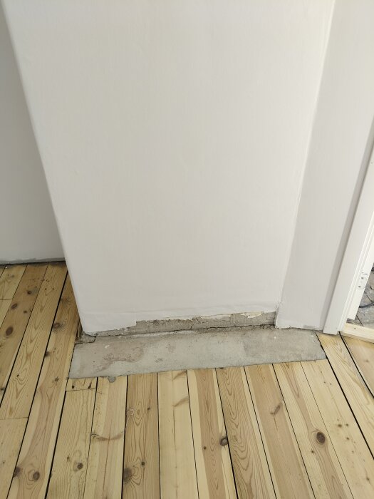 Träplankgolv med en rektangulär betongplatta mot murstocken, del av renoveringsprojekt i sovrum.