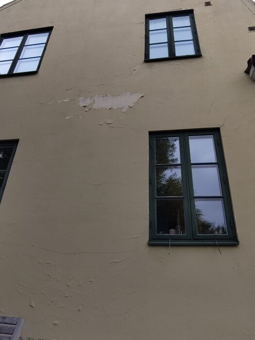Fasadvägg med flagnande färg och bubblor vid fönster, förmodligen på grund av felaktig målarfärg eller förberedelse.