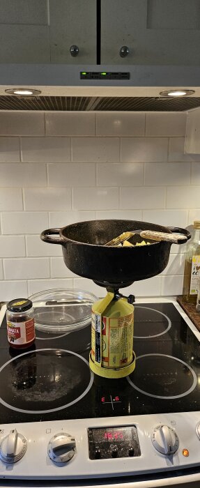 Spis med felmeddelande E6 och en gryta på en campinghäll placeras ovanpå hällen. En burk oliver syns bredvid.