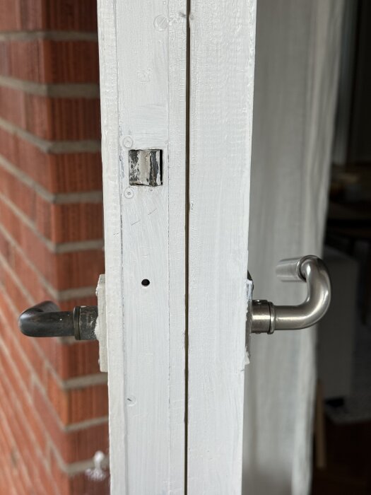 Vitmålad altandörr med metallhandtag, delvis öppnad, visar närbild av dörrkarmen. Fråga om Yale Code Handle-installation.