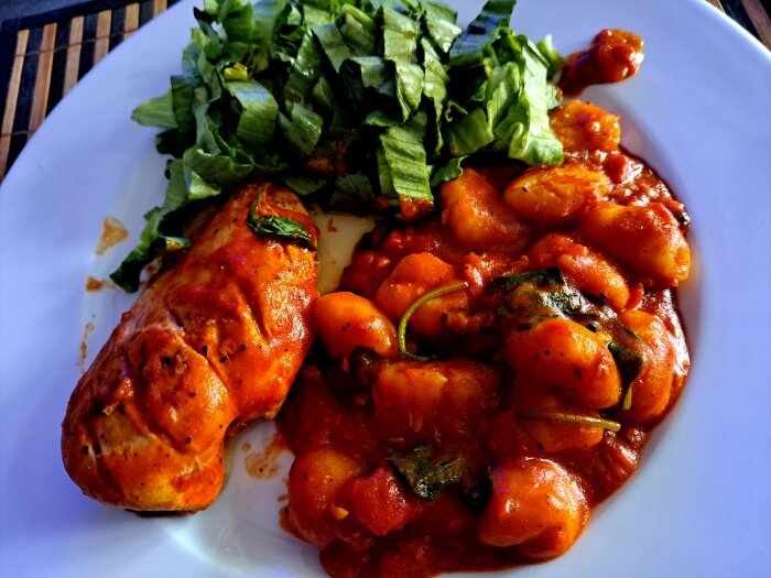 Kyckling i tomatsås med gnocchi och sallad på en vit tallrik.