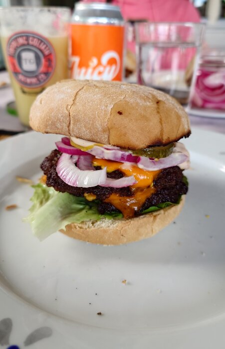 Hamburgare med Väddö cheddar, picklad rödlök, saltgurka, rostad lök, senap och ketchup på ICAs surdegsbröd, serverad på en tallrik.