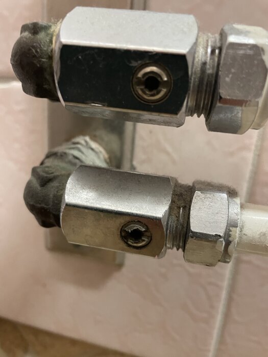 Kromade kopplingar och ventiler på vattenrör i badrum för avstängning, kräver verktyg.