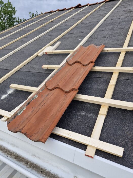 Orange takpanna på lutande tak med träreglar, skapar mellanrum mellan panna och underlag.
