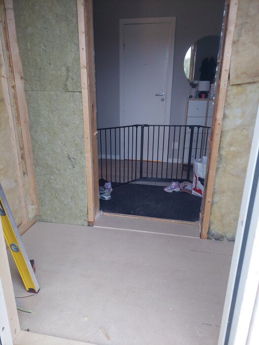 Husrenovering med ny ytterdörr och golv under uppbyggnad. Grind installerad i dörröppningen och byggmaterial synligt.