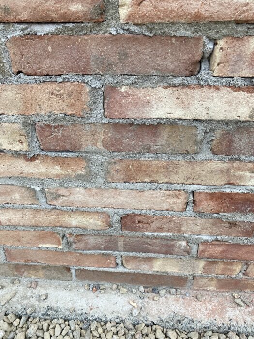 Tegelmur med slarviga fogar där vissa stenar inte är helt omslutna av murbruket, vilket ger ett gammaldags utseende.