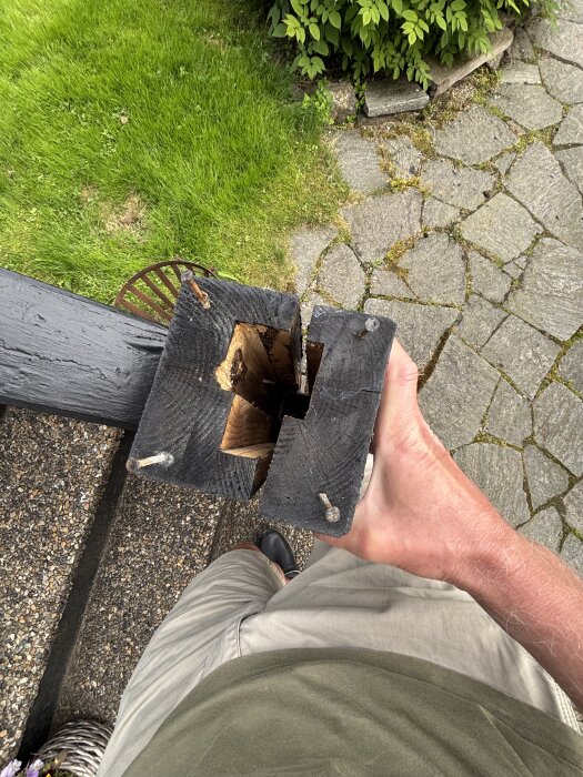 Svart trästolpe med urholkad insida och metalldelar, hålls i en hand ovanför en stengång.