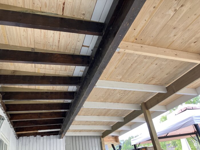 Under renovering av skärmtak med synliga bjälkar och finsågade brädor, delvis under byggnad, söks råd om isolering för uterum.