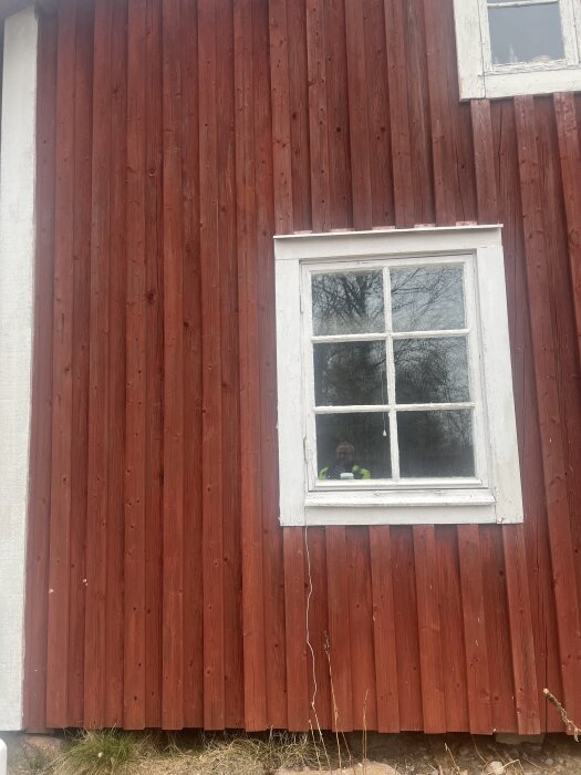 Röd fasad av 1890-talshus med vitmålat fönster, några paneler är spruckna. Fråga om lagning innan målning med falu rödfärg.