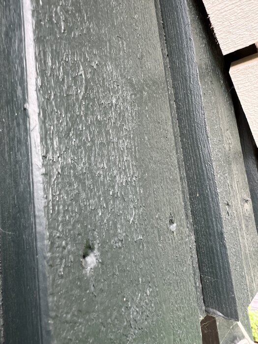 En närbild på en grönmålad trävägg med brädor som visar textur och slitage.