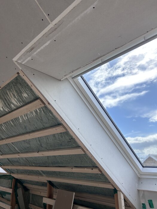 Gipsade fönstersmygar under takfönster, blå himmel utanför, del av pågående renovering inomhus.