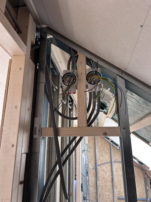 Byggarbete inomhus med synliga ledningar och elinstallationer på en vägg av träreglar.