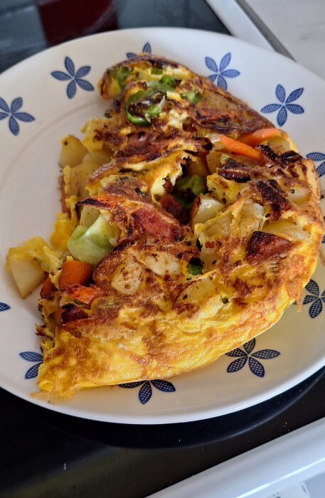Omelett med potatis, falukorv, lök, morot och vitkål på ett dekorerat fat.
