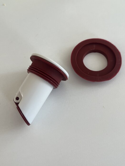 Vit backventil med röd packning bredvid på vit bakgrund, används för avfuktarlösning nära avloppsrör.