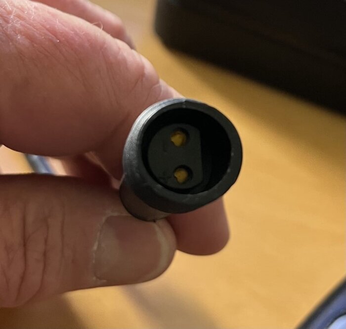 Svart kabelkontakt med två hål och rak kant, hålls i en hand.