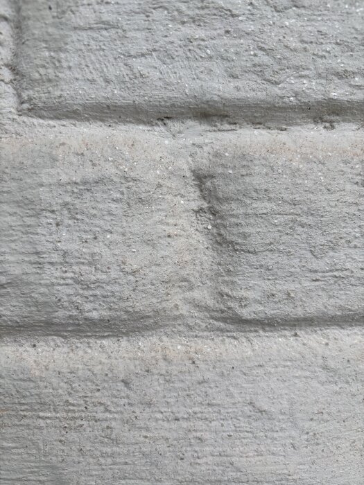 Närbild av fasadens slammade tegel från ett hus, med ett glittrande ytlager i solen som gör ytan mer levande.