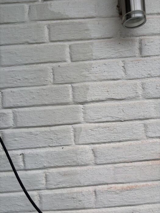 Målad tegelvägg med varierande nyans, delvis täckt av skimrande färglager med en lampa i övre högra hörnet.