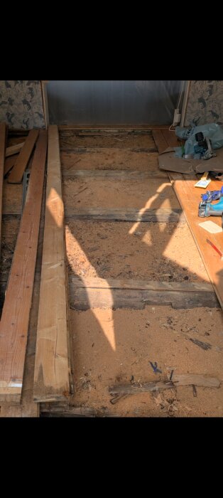 Golv med exponerade bjälkar, träplankor och sågspån i ett renoveringsprojekt av trossbotten i ett gammalt hus.