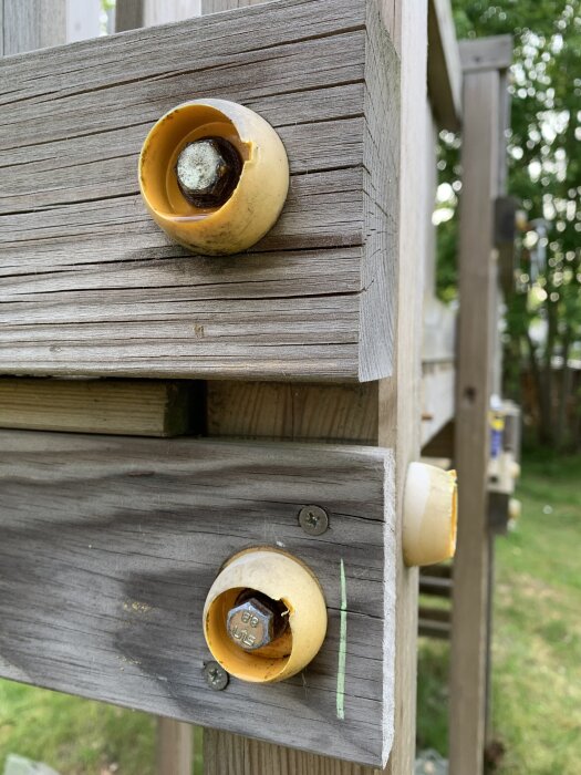 Gammal klätterställning med vägg av trä där rostiga bultar delvis täcks av gula plastskydd.