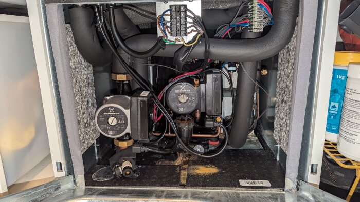 Cirkulationspumpar och anslutna rör i ett ventilerat skåp med synliga elektriska kablar och komponenter.