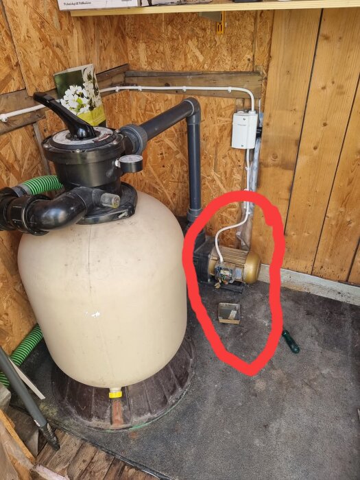Guldigt trasigt motor intill en tank i ett träfförråd, markerat med en röd cirkel, mot en panelvägg.