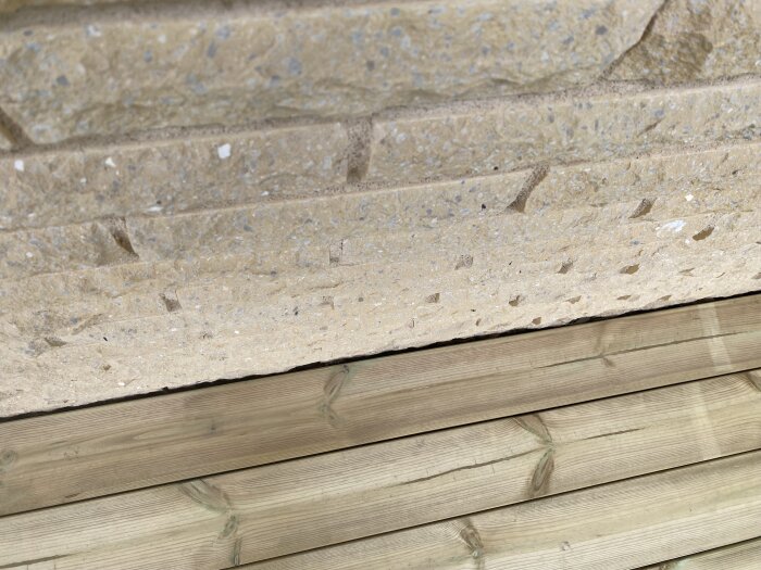 Trätrall med ojämn glipa mot vägg av huggen mexitegel på altan, visar möjlig monteringsutmaning för jämn fogning.