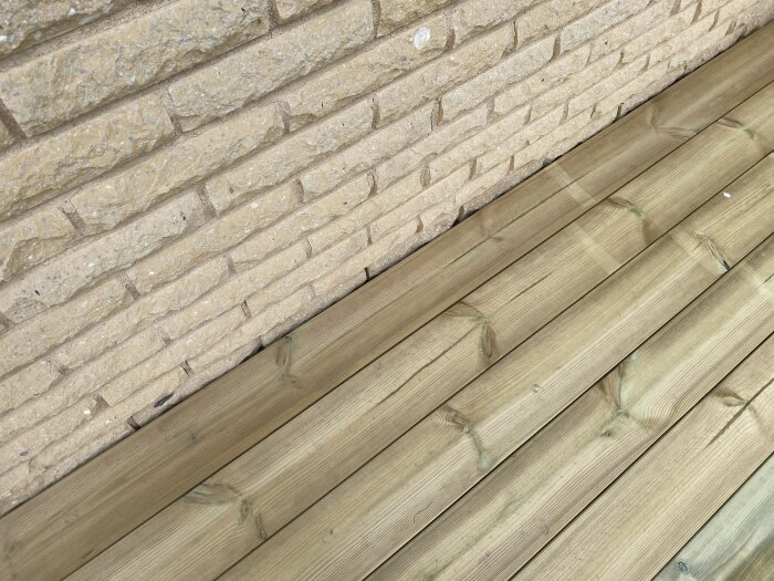 Trätrall mot vägg i huggen mexitegel, synlig glipa mellan trall och tegel. Diskuteras om att lägga regel eller justera springa för jämn finish.