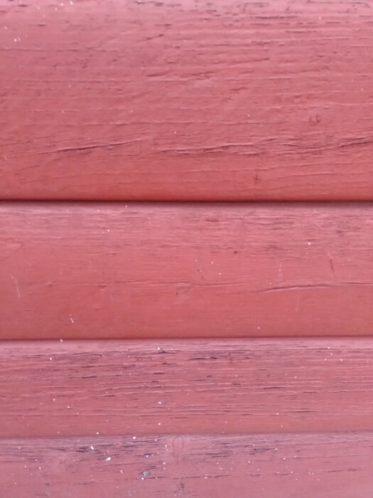 Röd fasad med träpanel, färgen verkar plastig och spröd. Brännprov på färgflaga utfördes för att identifiera färgtypen, misstänkt akrylat- eller oljefärg.