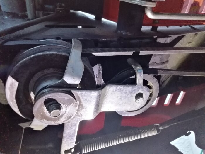 En rem är korrekt monterad runt remspännaren på ett klippdäck, med metallkomponenter synliga i närbild.