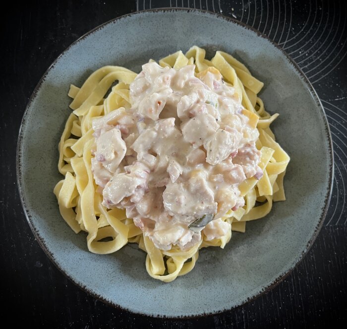 Pastasås med kyckling, bacon, chili, blomkål, lök och paprika på färsk pasta på en grå tallrik.